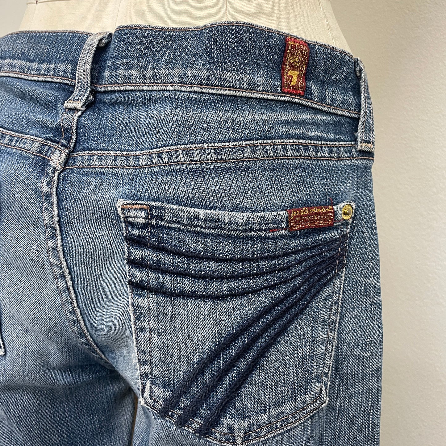 Close-up of blue jeans with a 7 for all mankind brand logo on a neutral background