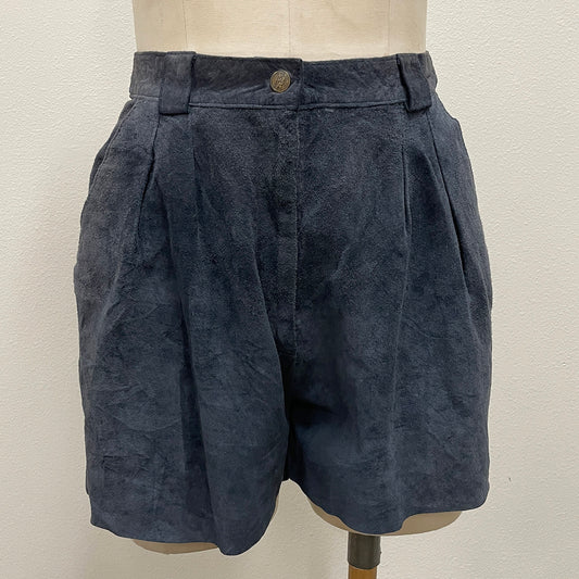 Dark blue suede shorts displayed on a cream-colored mannequin torso against a plain off-white wall.