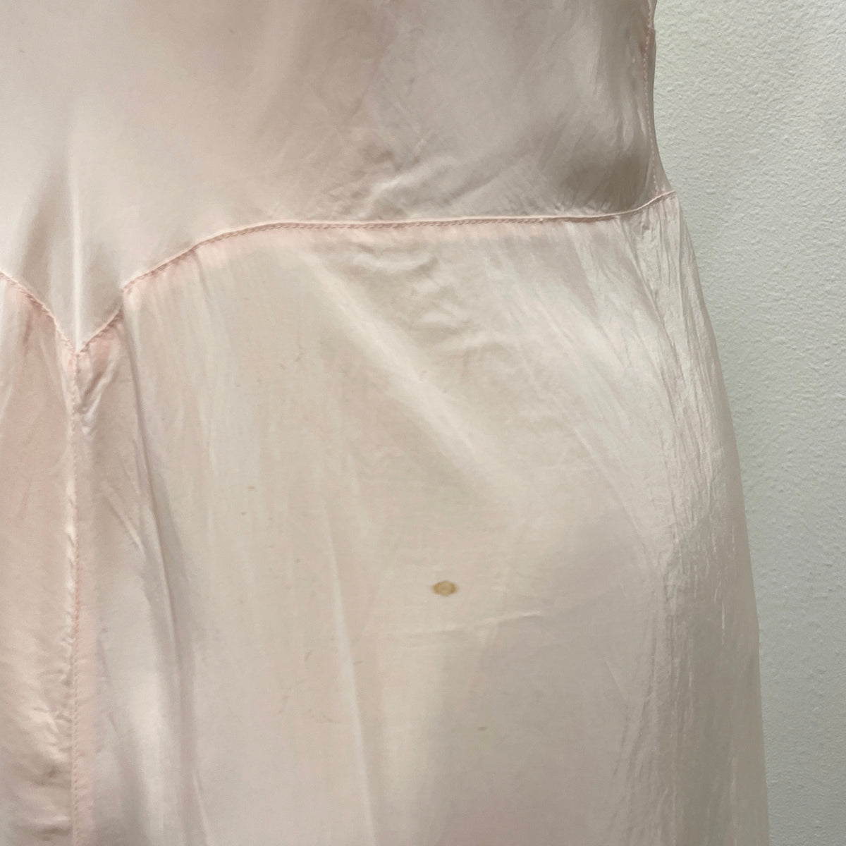 A close-up of a light beige stain on silky slip dress at back, set against a plain white wall.