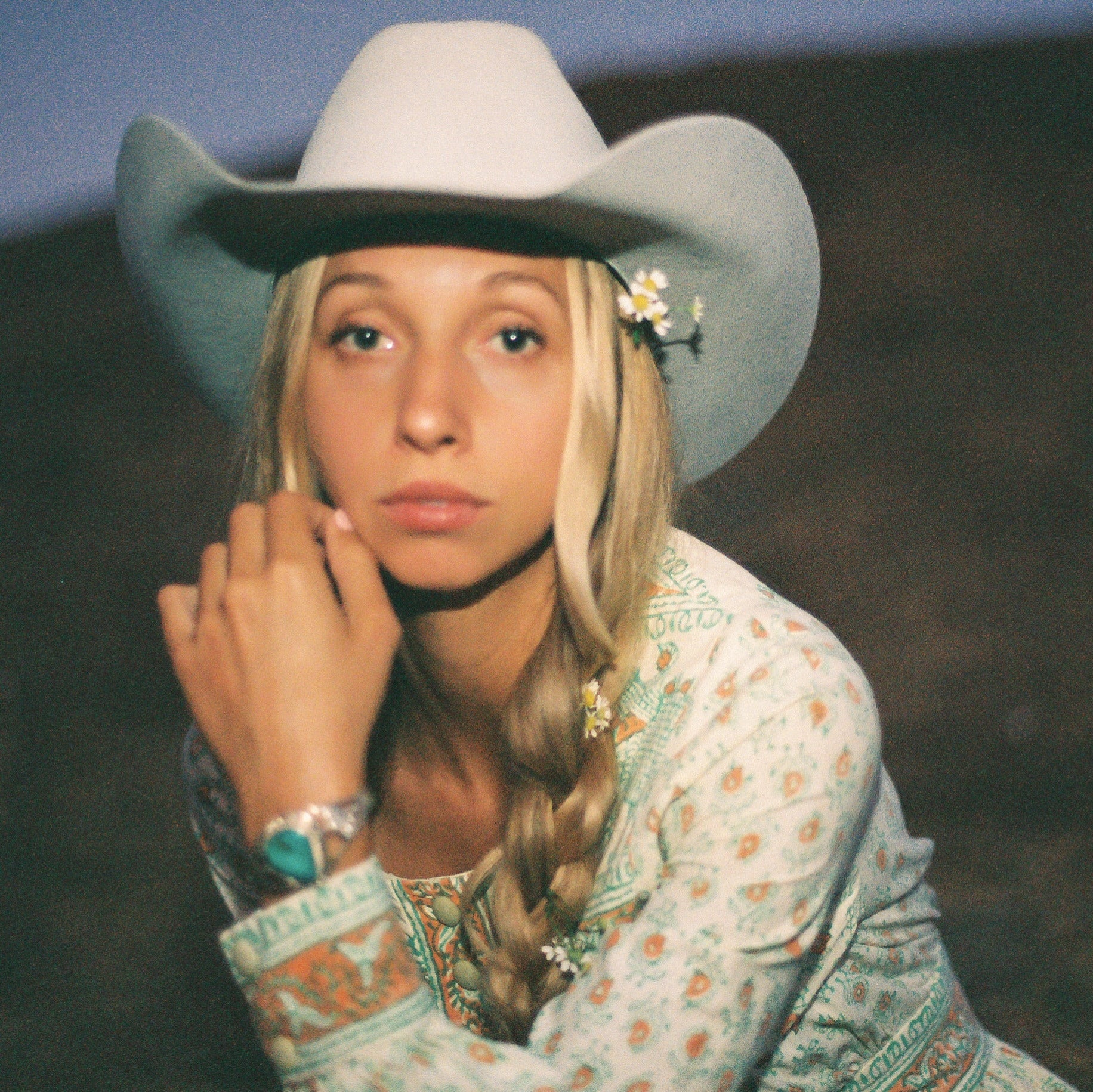 Woman wearing a cowboy hat and patterned floral dress against a dark background