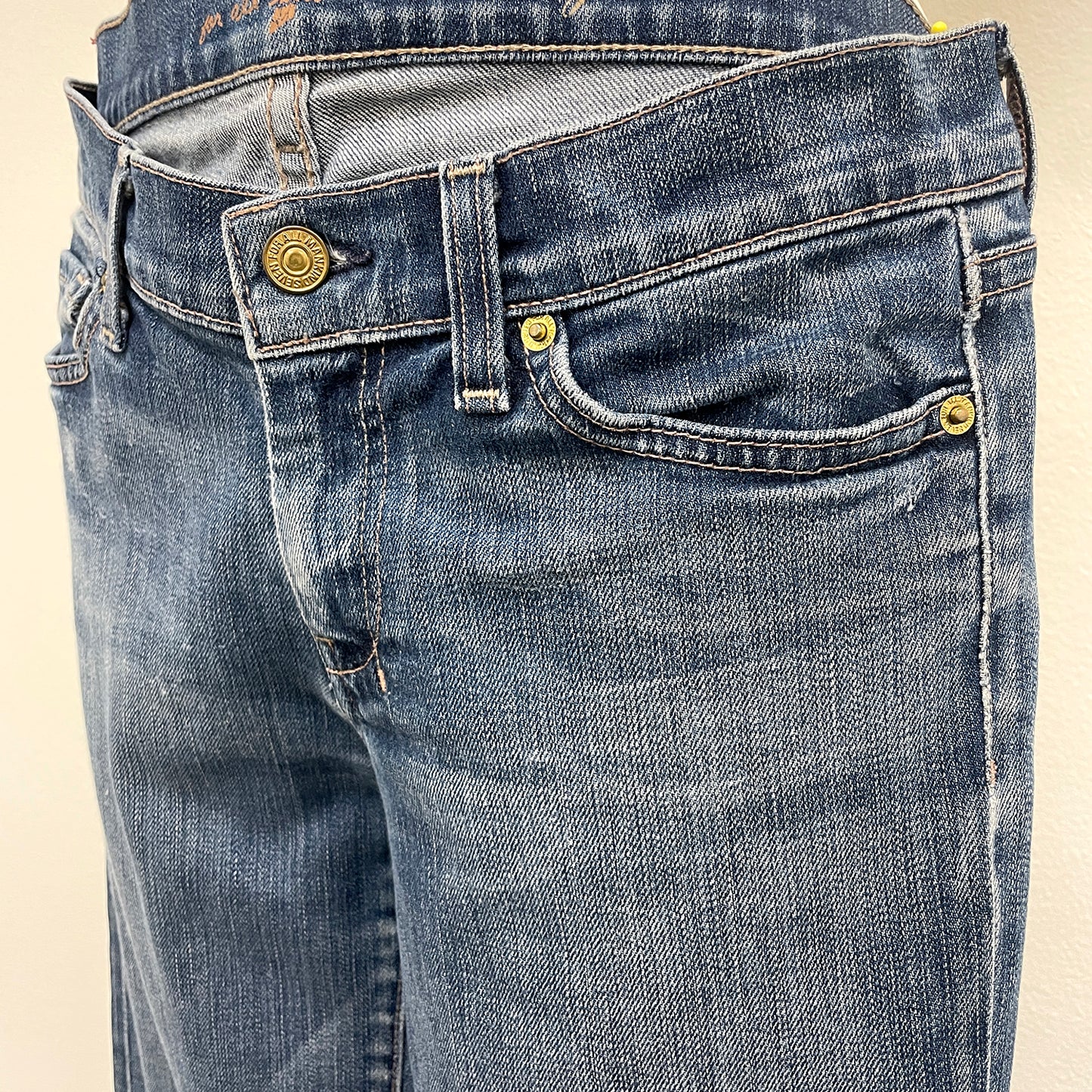 Close-up of blue jeans with gold buttons on a beige background