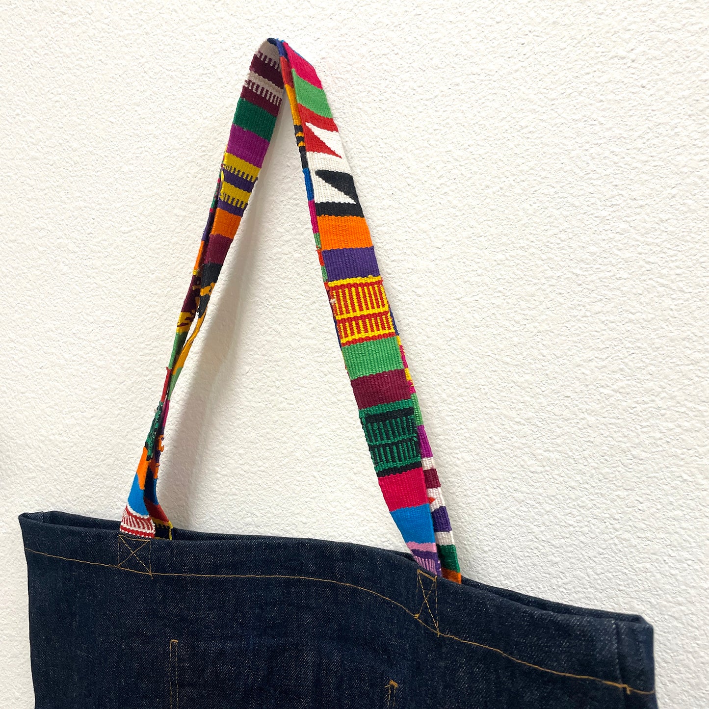 Dark blue tote bag with a colorful striped handle on a white background
