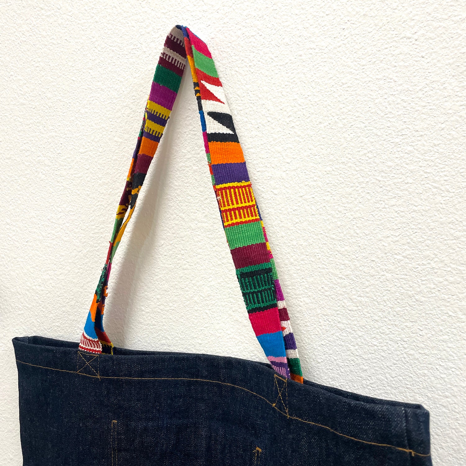 Dark blue tote bag with a colorful striped handle on a white background