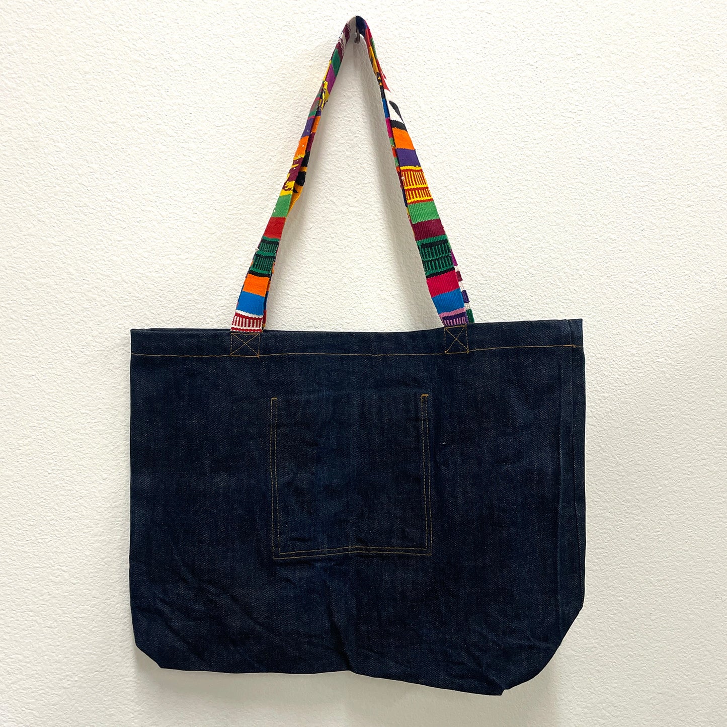 Dark denim tote bag with colorful handle on a white background