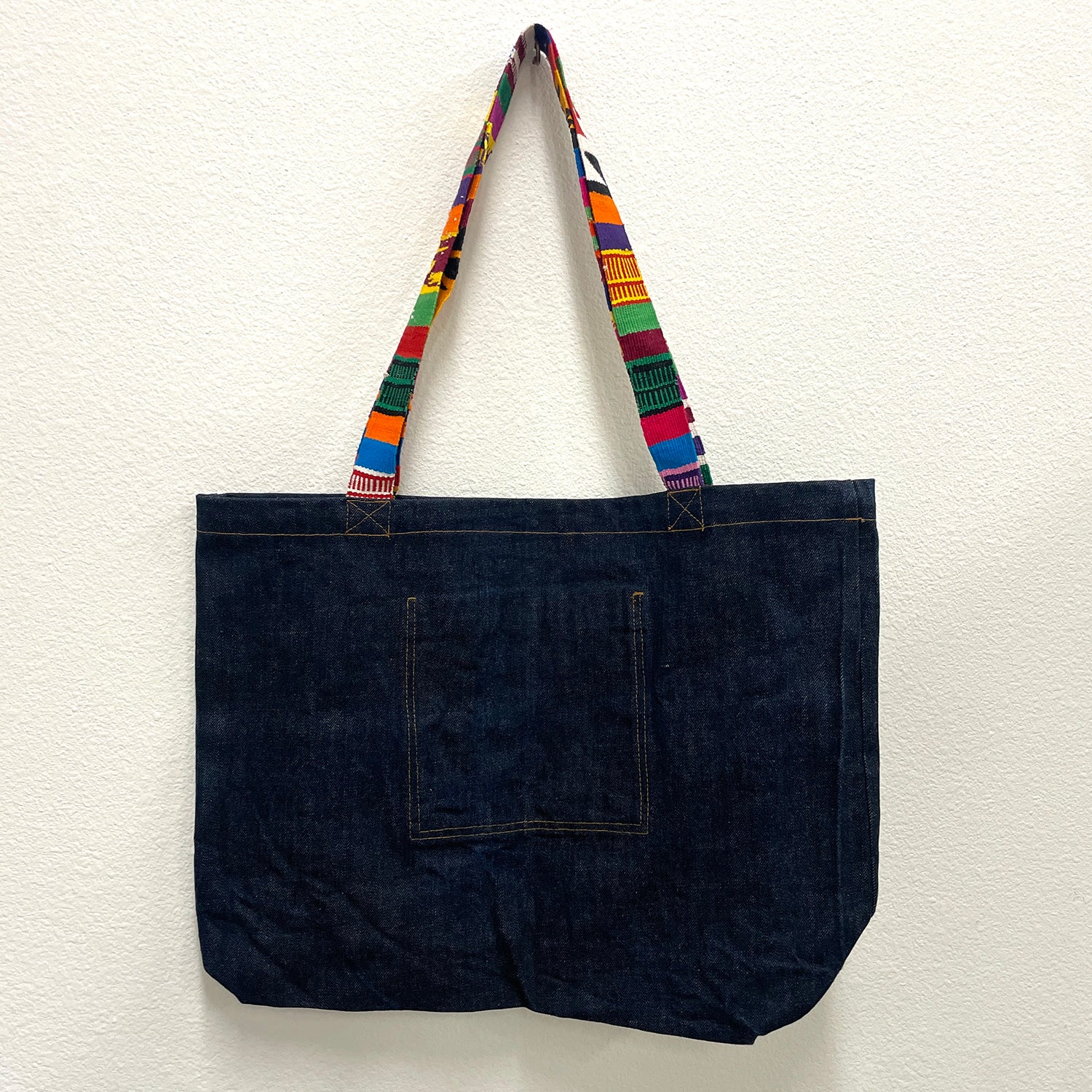 Dark denim tote bag with colorful handle on a white background