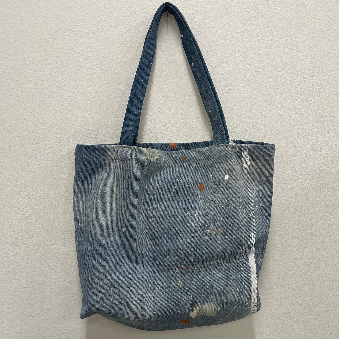 Blue denim tote bag with paint splatters on a white background