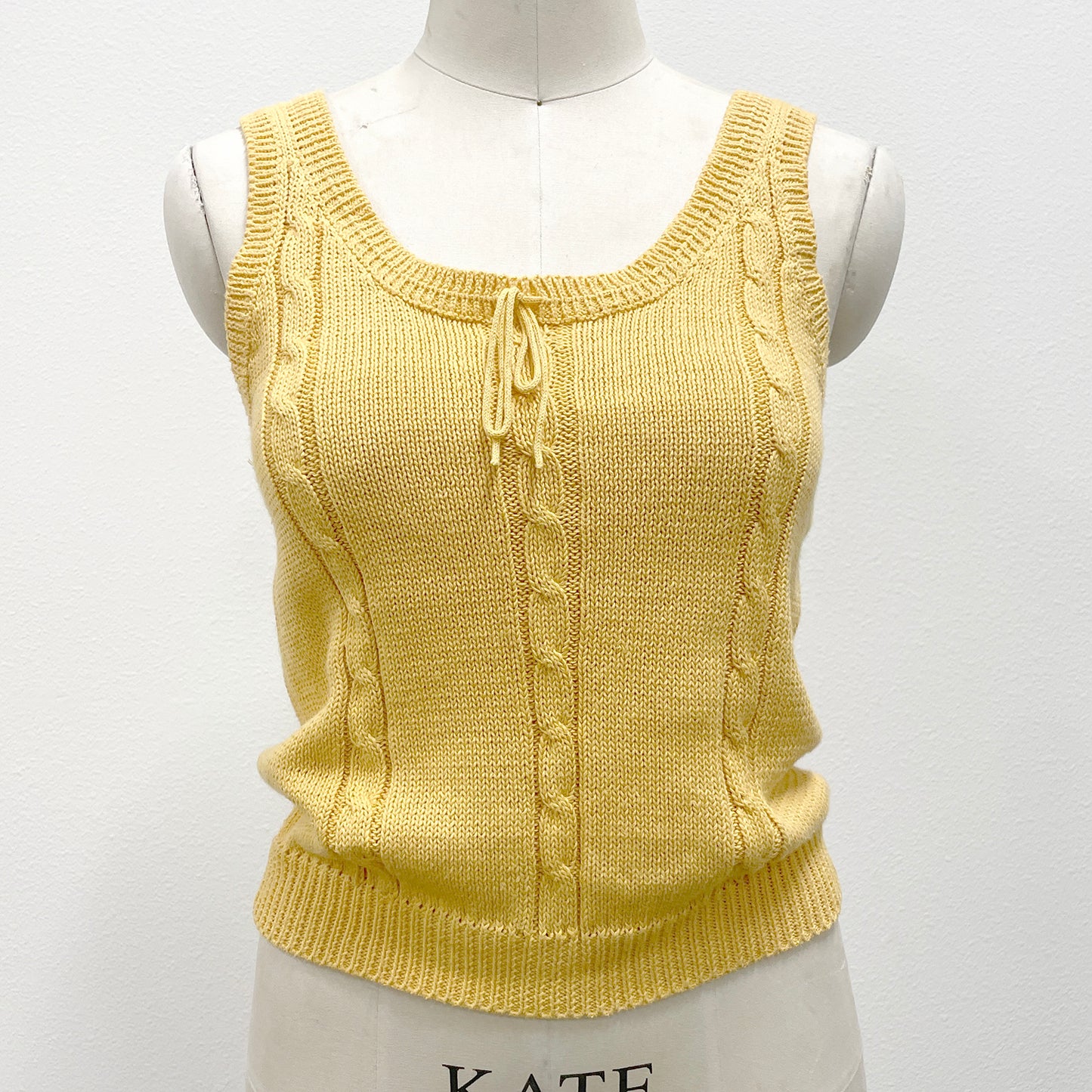Yellow knitted sleeveless sweater tank on a mannequin against a white background