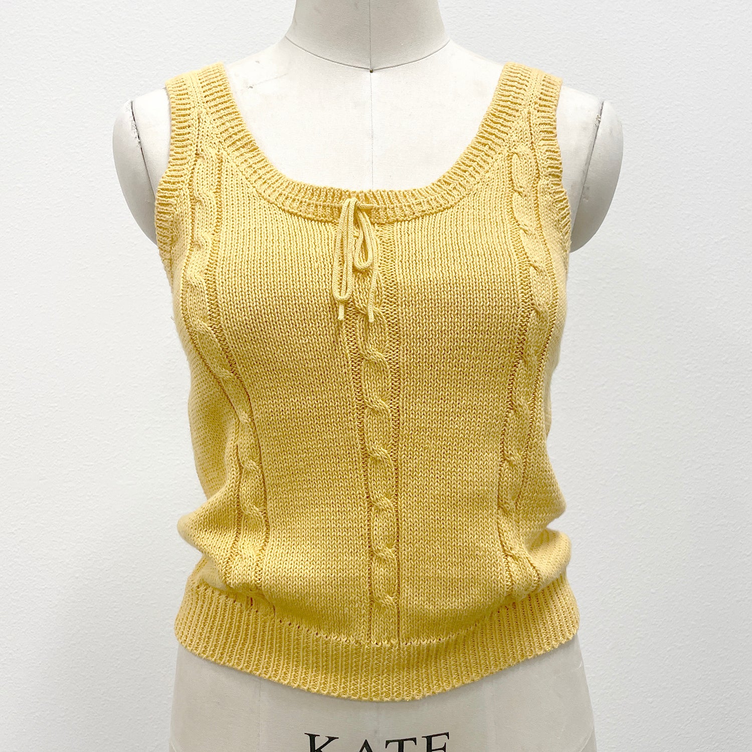 Yellow knitted sleeveless sweater tank on a mannequin against a white background