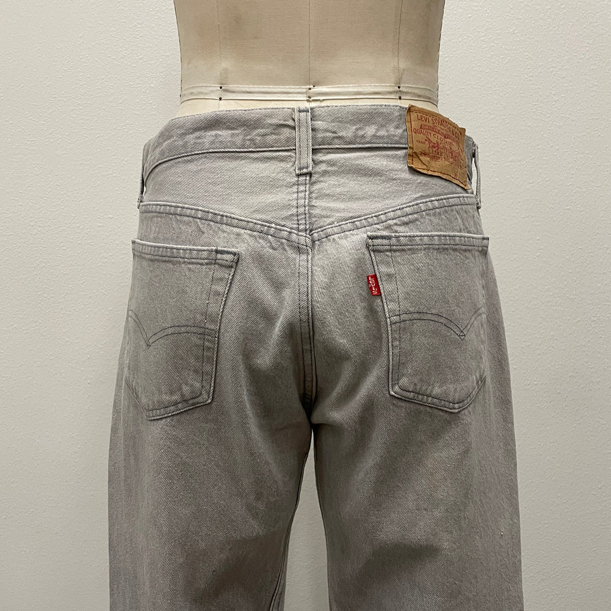 Rear view of light gray Levi's jeans on a dress form mannequin, showing the back pockets, leather patch, and red tab.