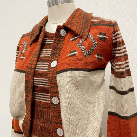 A vintage knit cardigan sweater displayed on a mannequin torso. The cardigan features a warm rust-orange and cream color-blocked design with geometric patterns, striped details, and pearlized buttons.