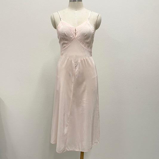 A light pink silky slip dress displayed on a cream mannequin torso against a plain off-white wall.