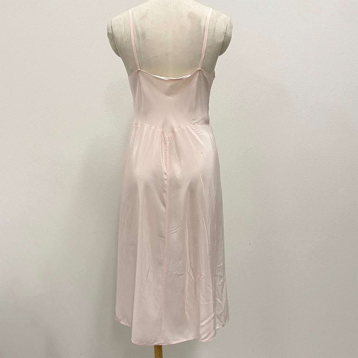 A light pink silky slip dress displayed on a cream-colored dress form mannequin against a plain white wall.