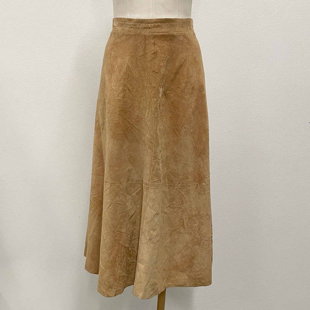 A tan suede A-line midi skirt displayed on a mannequin torso against a white wall.