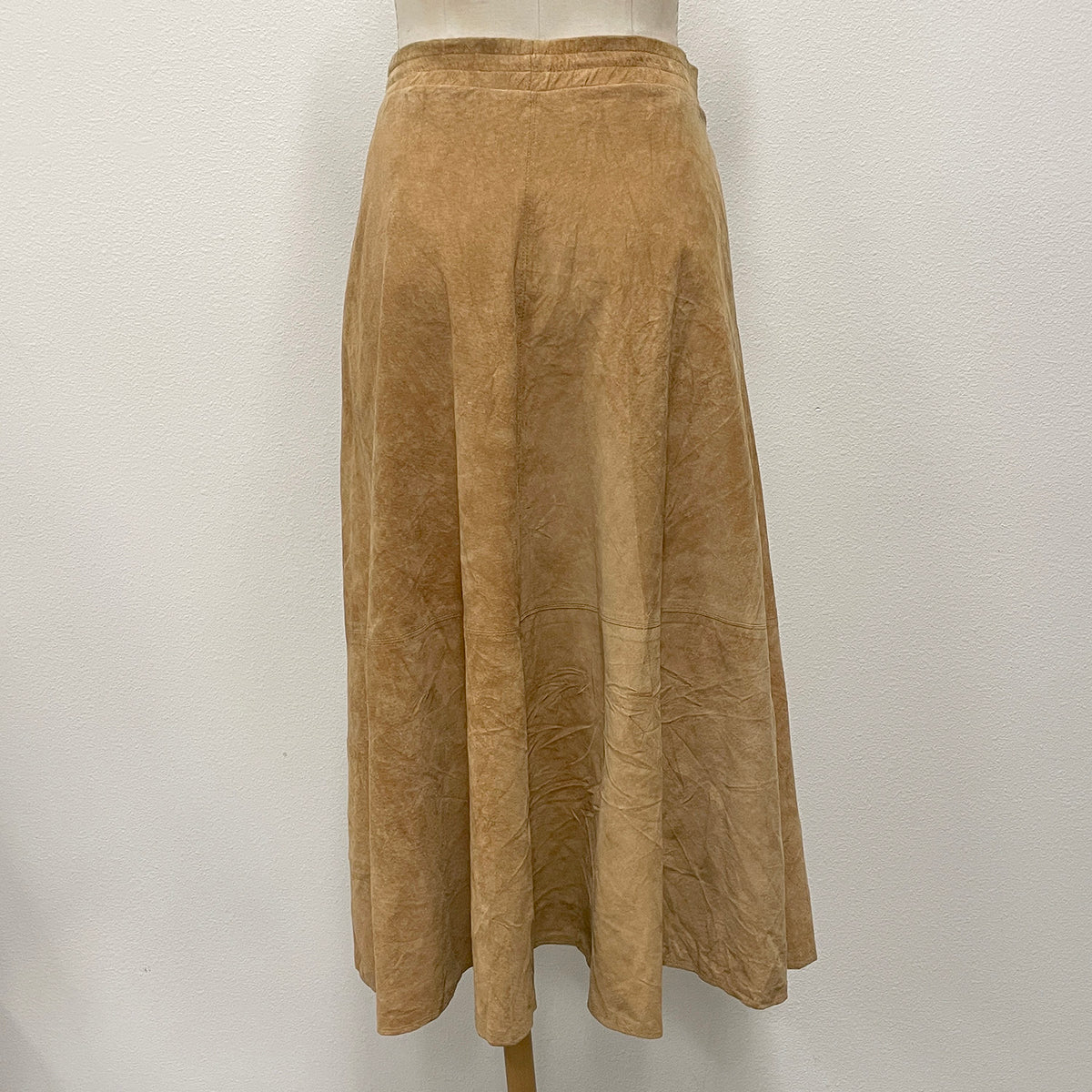 A tan suede A-line midi skirt displayed on a mannequin torso against a white wall.