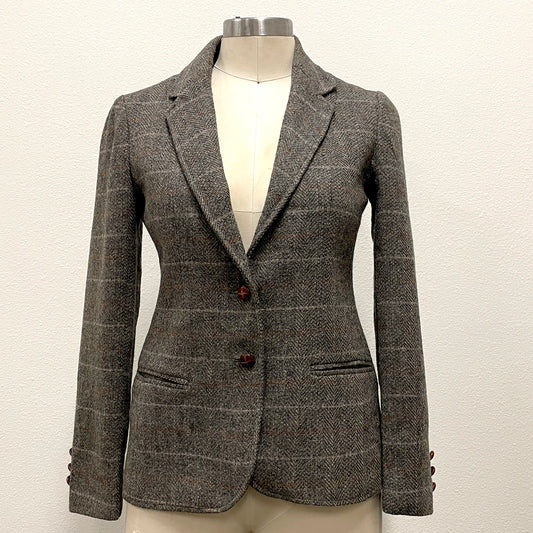 A gray and brown tweed blazer with a subtle windowpane check pattern, displayed on a cream-colored mannequin torso. The blazer features notch lapels, a two-button front closure, and welt pockets.