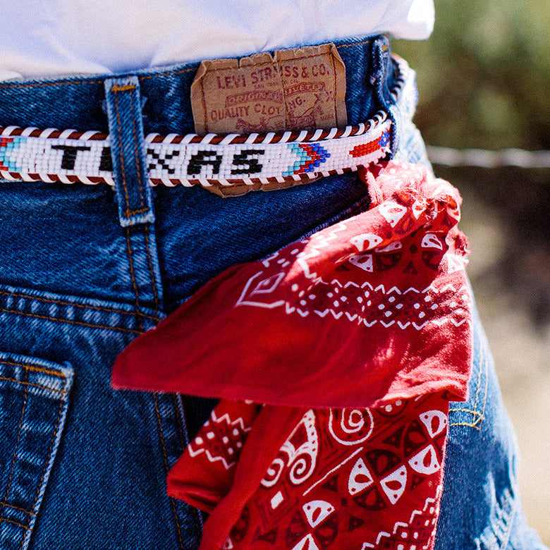 Person wearing blue jeans with a patterned belt and red bandana, outdoors.